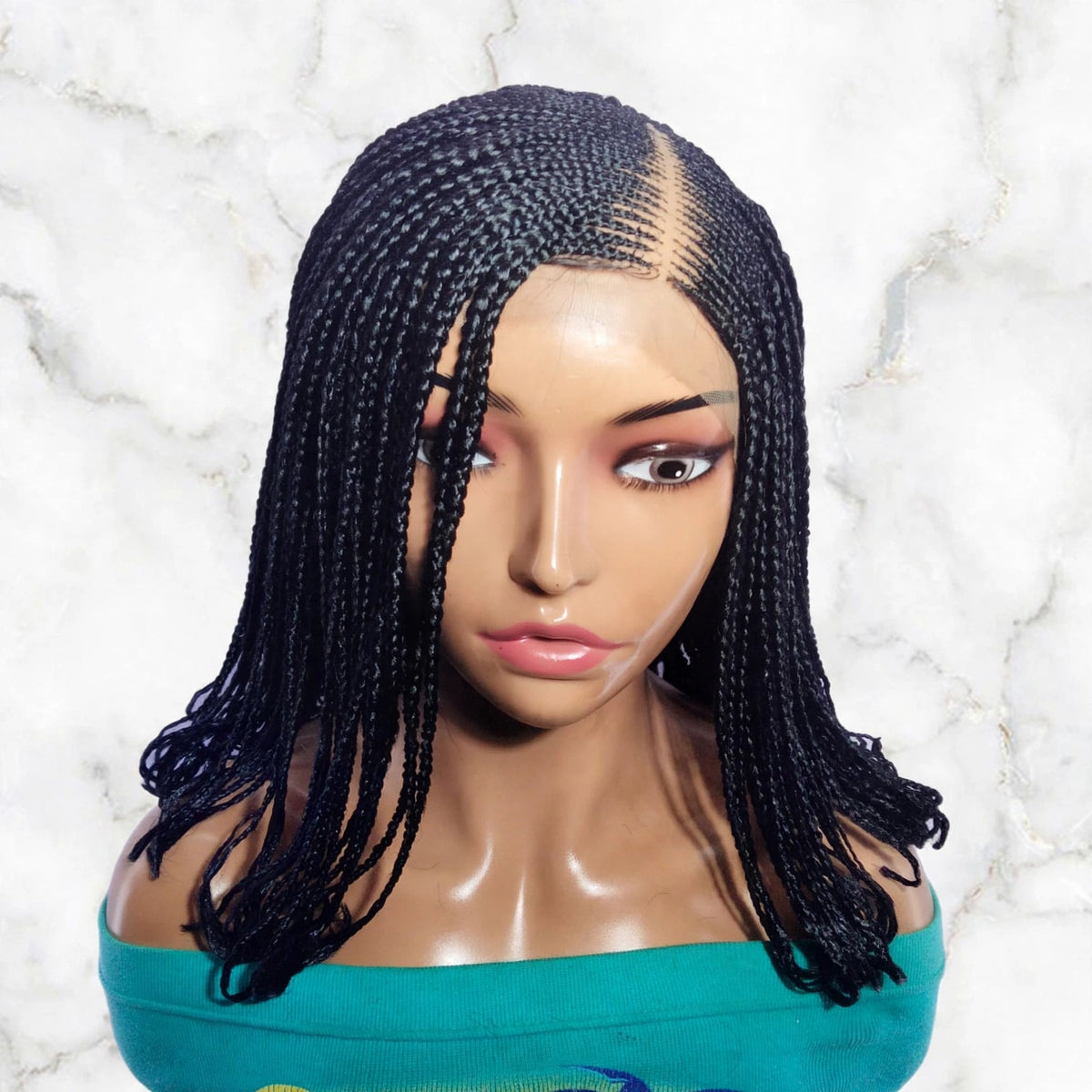 Black braided wig with long box braids styled in a center part, displayed on a female mannequin bust against a white marble background.
